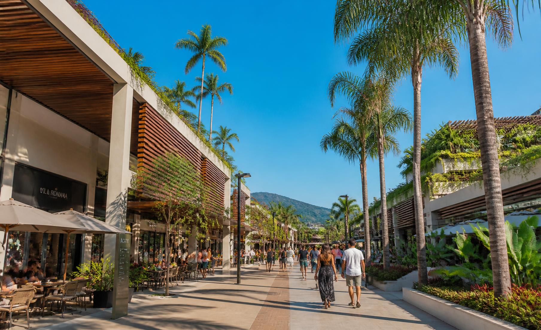 Boulevard a céu aberto do MULTI Open Shopping com palmeiras, arquitetura em madeira e pessoas circulando